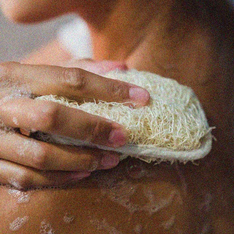 Woman applying Temazcal Life botanical exfoliating soap with a bath loofah.