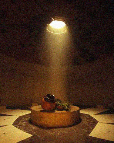 Interior of an empty temazcal with skylight shedding light into the center of the temazcal.